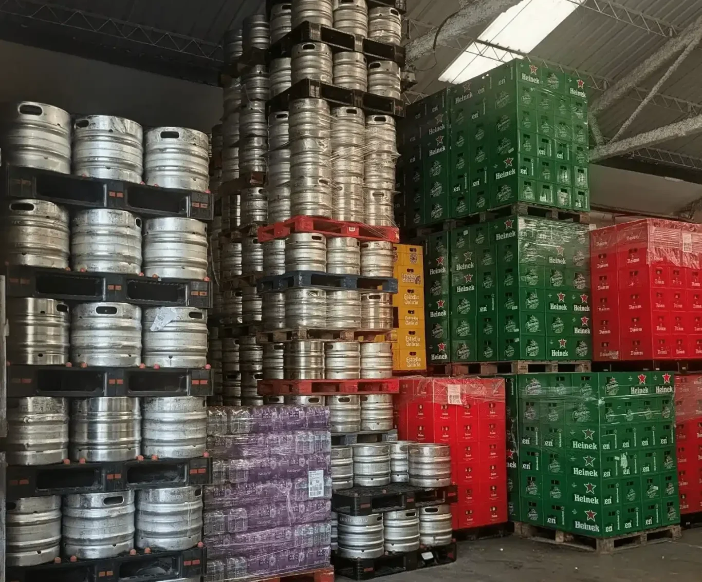 Almacén central de Bebidas Barcino Estanterías altas con cajas verdes de heineken y rojas de estrella damm apiladas en un almacén.