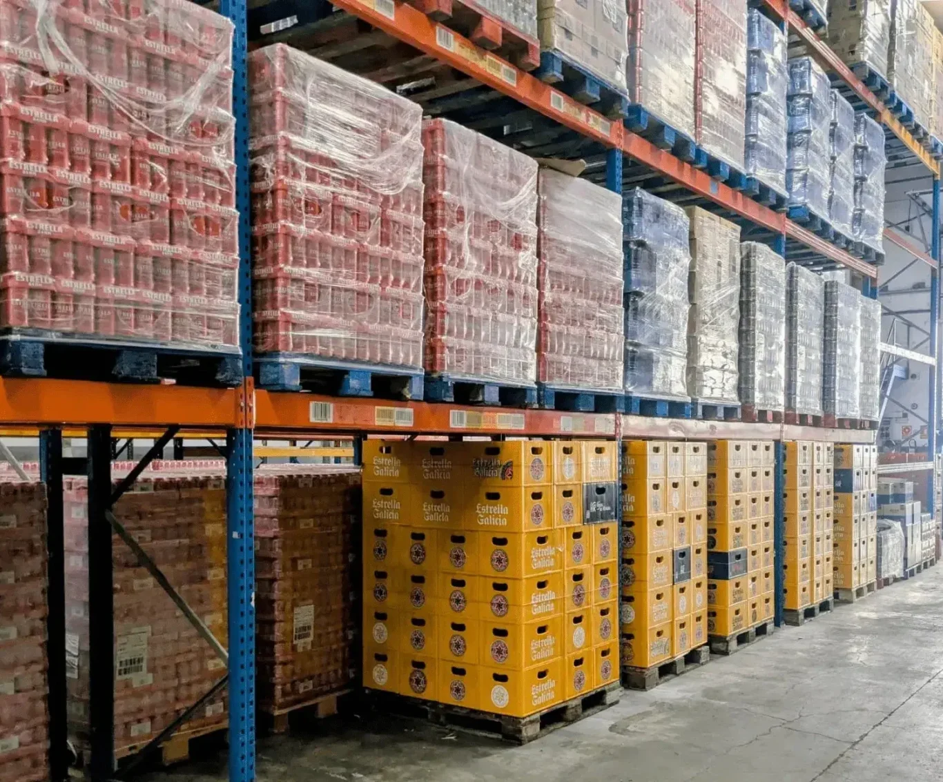 Almacén central de Bebidas Barcino Estanterías altas con cajas verdes de heineken y rojas de estrella damm apiladas en un almacén.